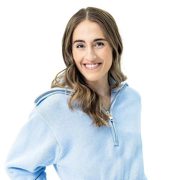 Sabrina, wearing a light blue zip up hoodie with one hand on her hip, looking at the camera, smiling