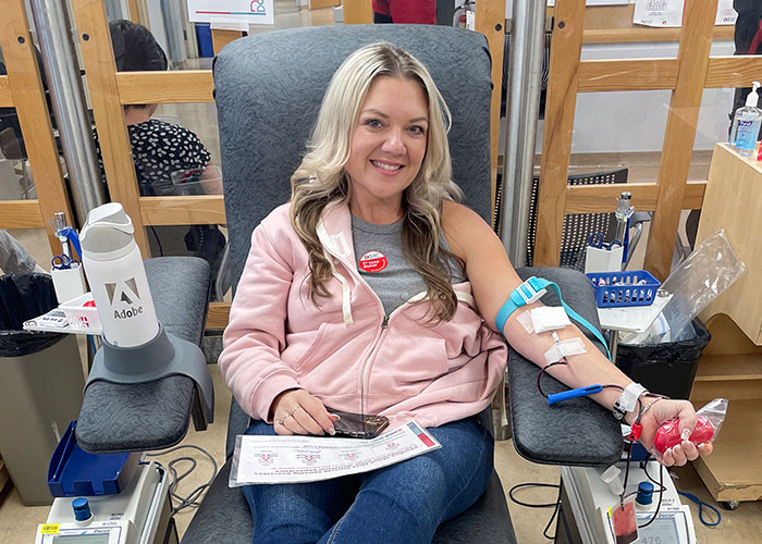 A woman wearing a pink sweater sitting in a donation chair giving blood.