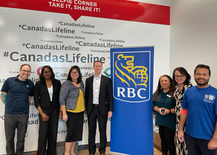 Group of people smiling in front of a Canadian Blood Services selfie wall, beside a pop-up banner with RBC’s logo.