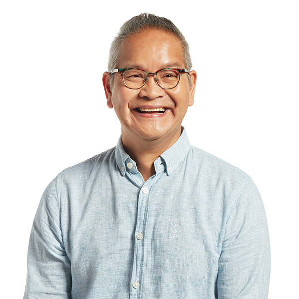 Tom, wearing a light blue button up shirt and glasses,looking at the camera, smiling