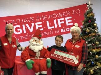 Canadian Blood Services Volunteers stand with a little boy holding a Gives Life Together sign during Christmas