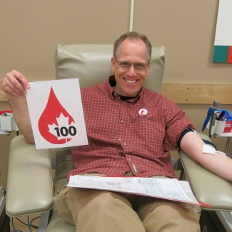 Blood donor holding sign featuring a blood drop and number 100