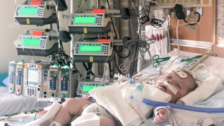 Image of baby blood recipient Madison Lewis in the hospital bed with tube attached to her recovering from surgery