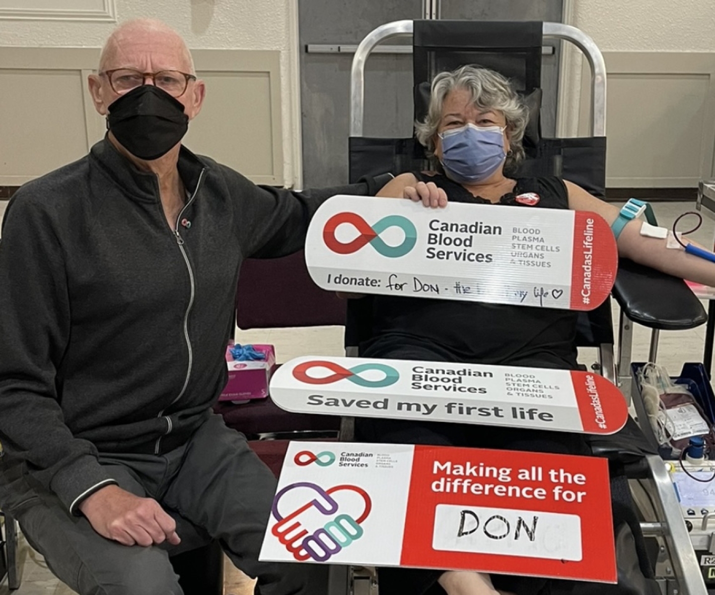 Blood donor in chair holding signs