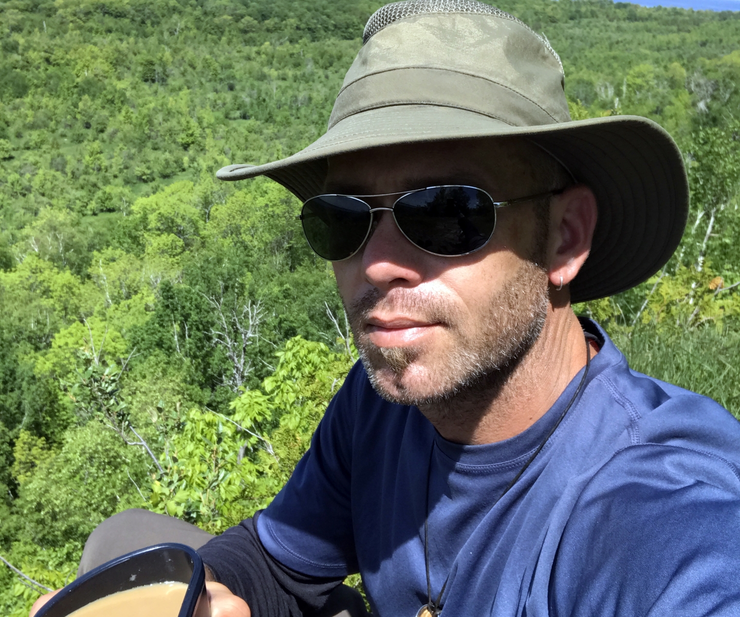 Man in hat and sunglasses outdoors with coffee cup