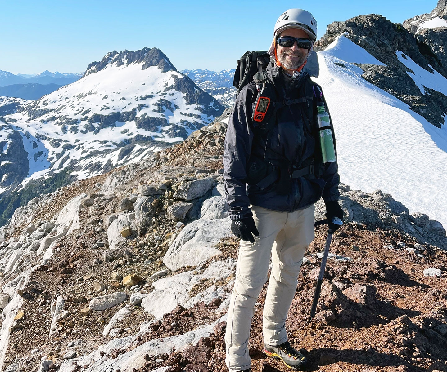 Un homme portant des lunettes de soleil et un casque dans un paysage de sommets montagneux.