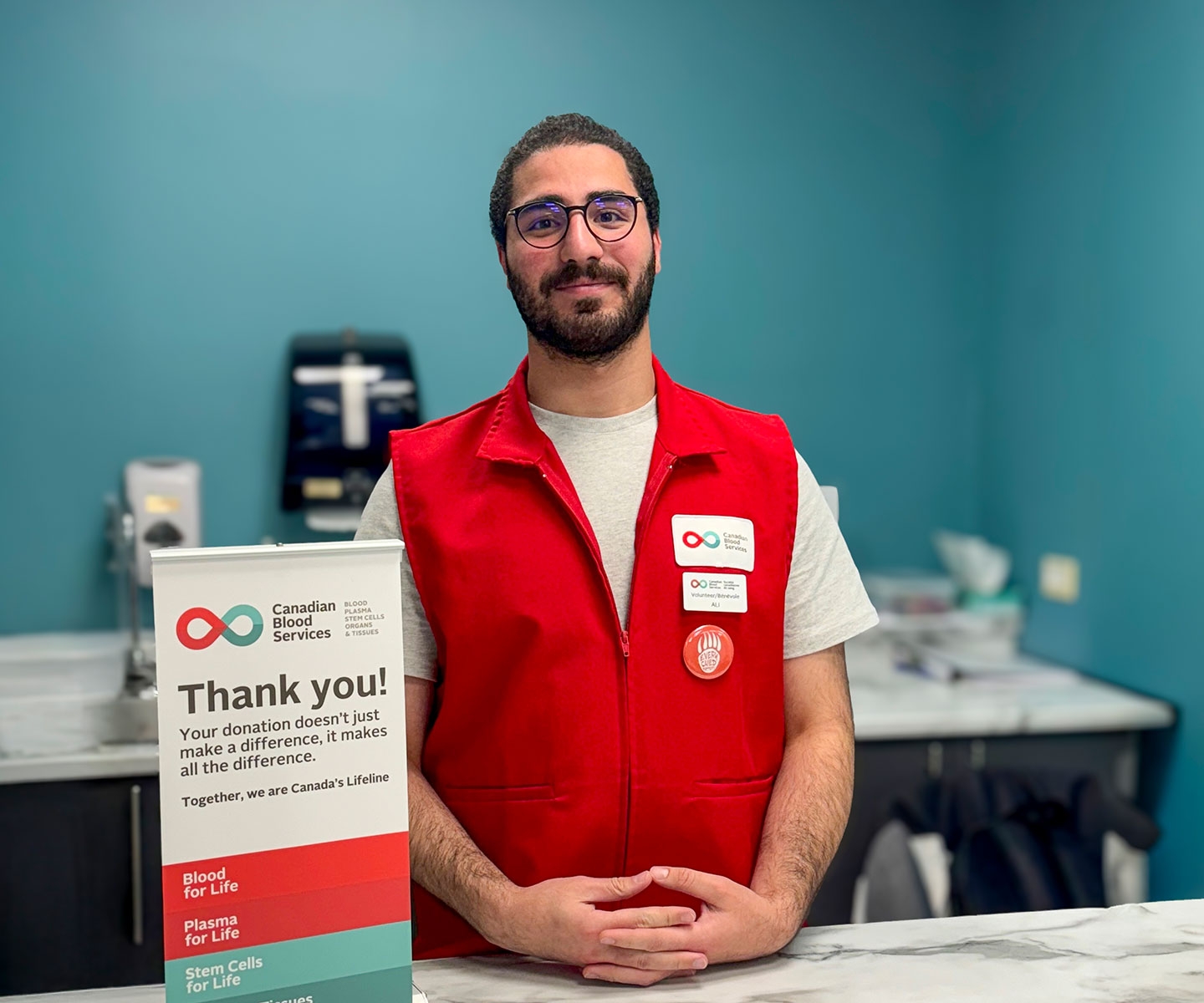Young man wearing a red volunteer vest standing behind a refreshment counter