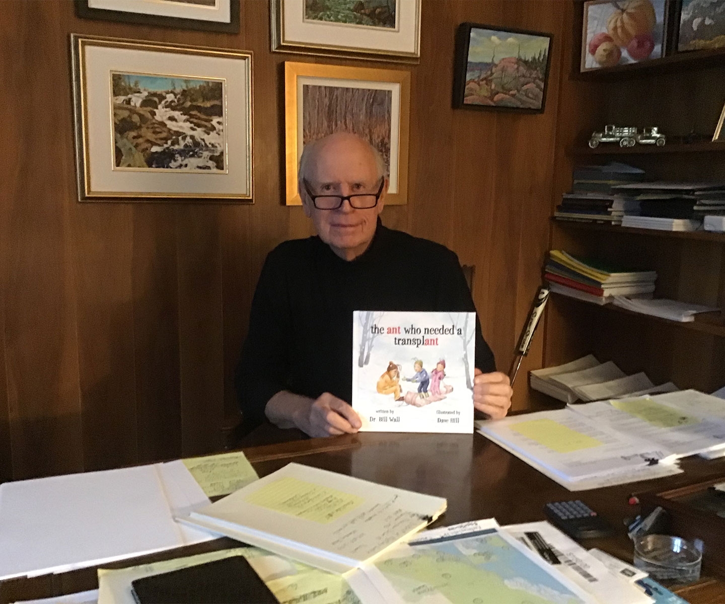 Dr Wall à son bureau tenant un exemplaire de son livre pour enfants intitulé the ant who needed a transplant.