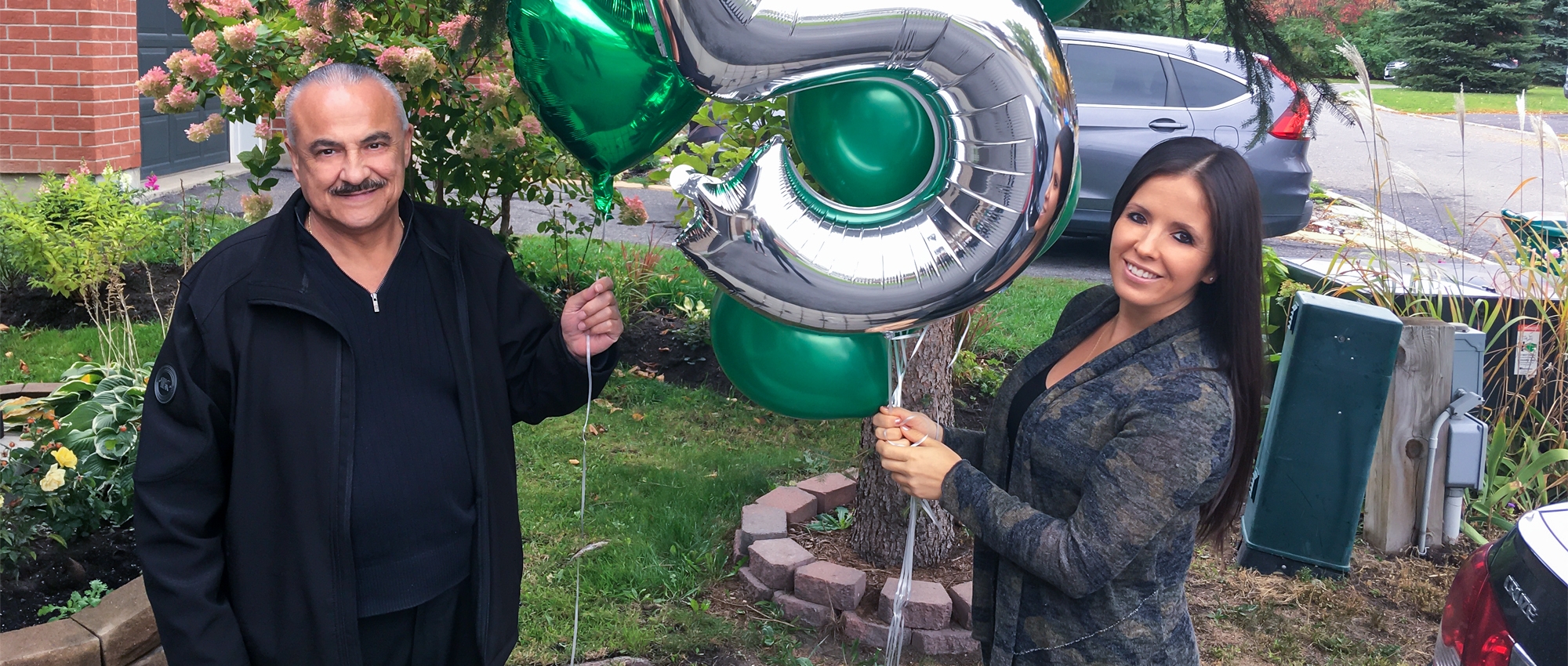 Featured image of Jenn and Tony outside on the lawn holding numbered balloons