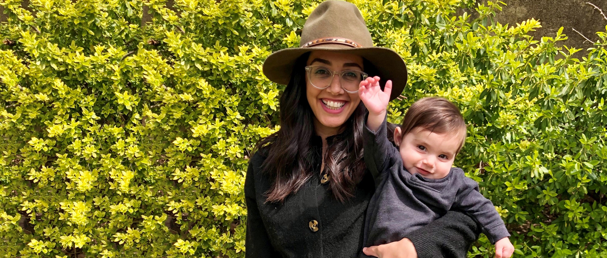 A young woman in a wide-brimmed hat smiles broadly as she holds her baby son.