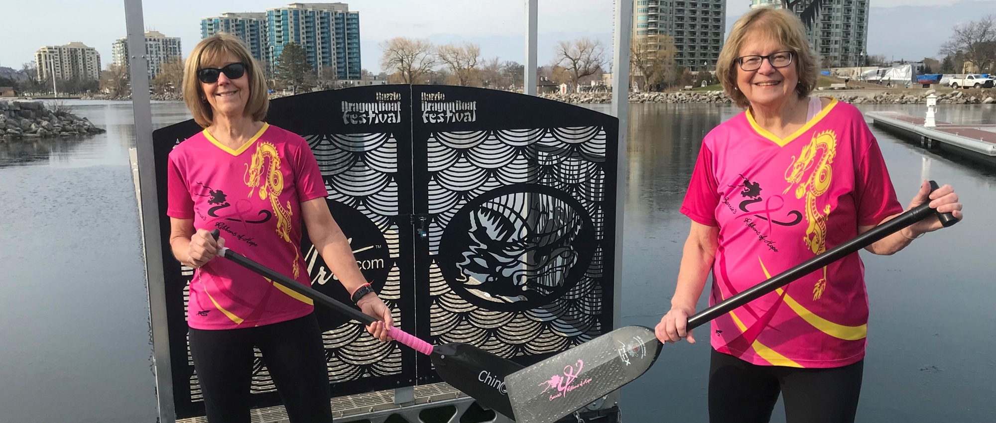 Breast cancer survivors and dragon boat team members Vonnie Pope and Donna Jelly with paddles near the water.