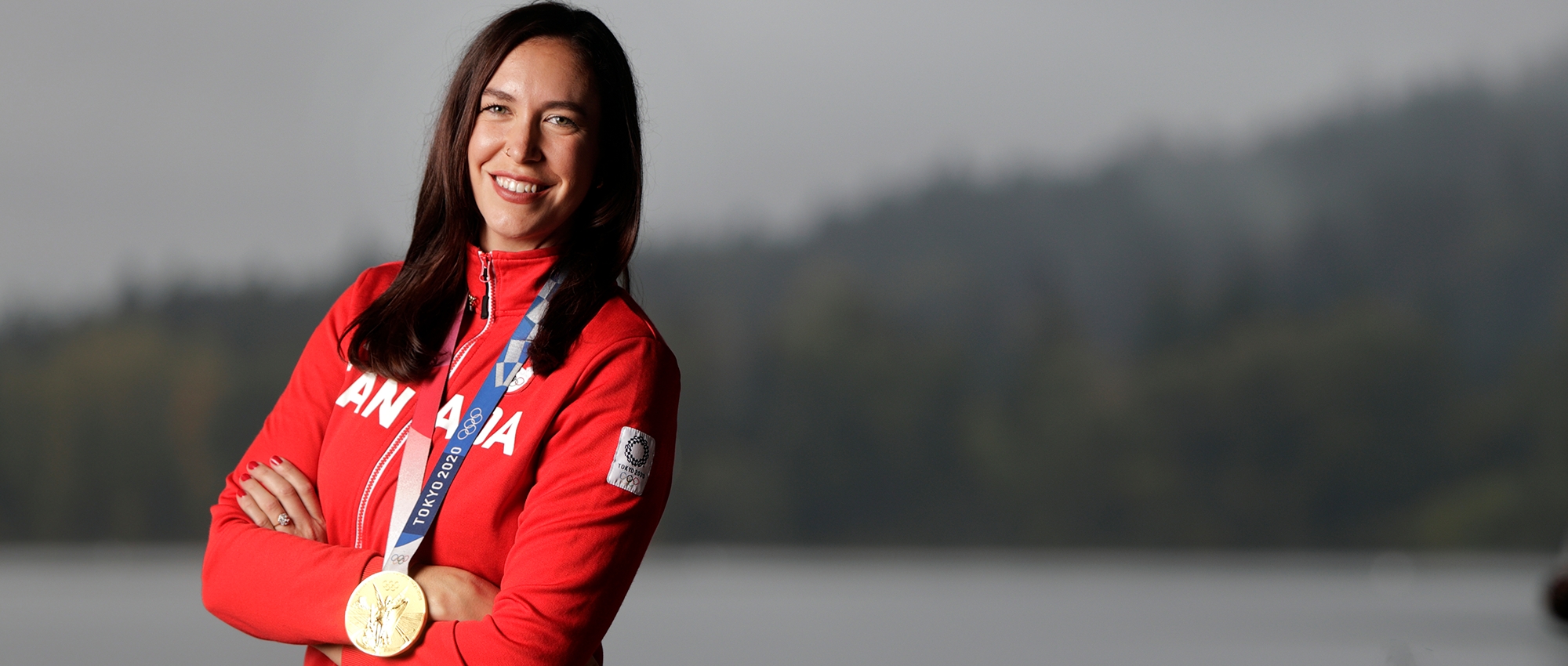 Andrea Proske wears Olympic gold medal near lake and trees 