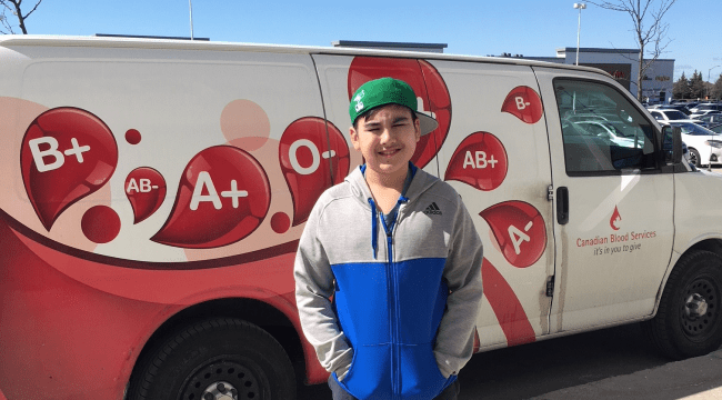 Aary with a green baseball cap standing in front of a Canadian Blood Services van outside