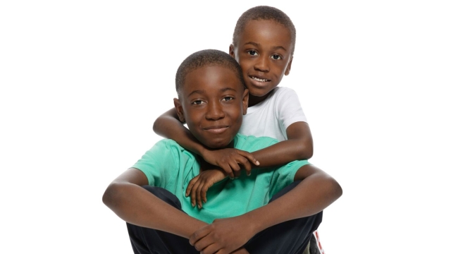 Older brother sitting cross-legged with younger brother hugging him from behind.