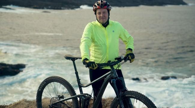 Man in yellow jacket stands with bicycle near ocean