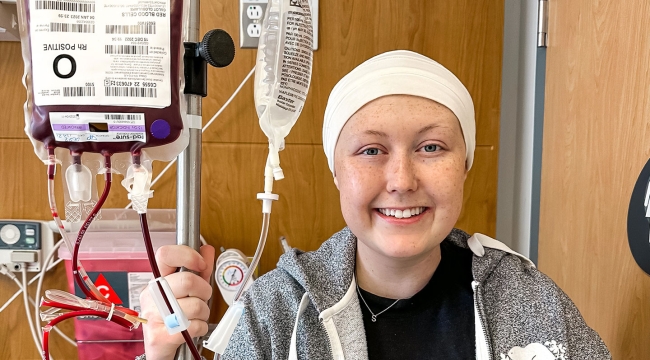 Shae-Lynn, souriante, la main droite autour d’un support de perfusion pendant qu’elle reçoit du sang.