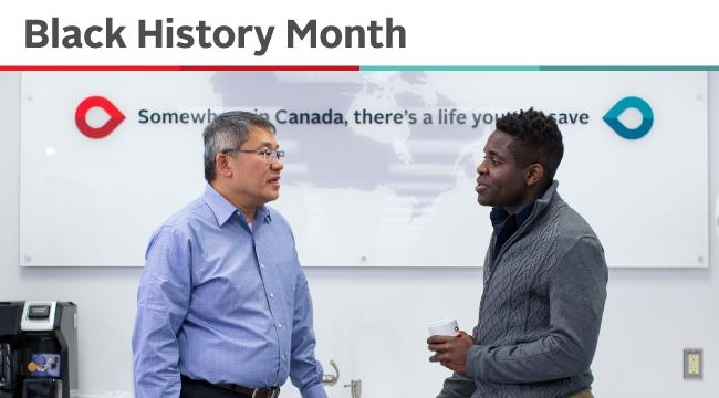 An Asian employee and a Black employee in conversation. Behind them is a map of Canada with the words Somewhere in Canada there’s a life you can save.
