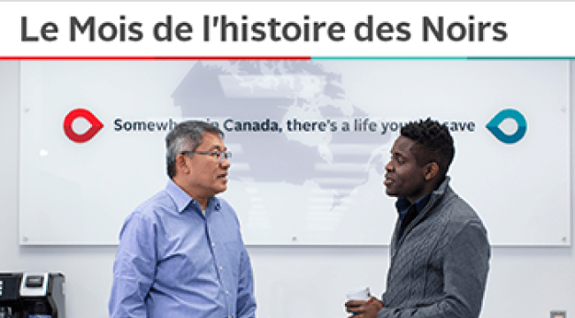 An Asian employee and a Black employee in conversation. Behind them is a map of Canada with the words Somewhere in Canada there’s a life you can save.