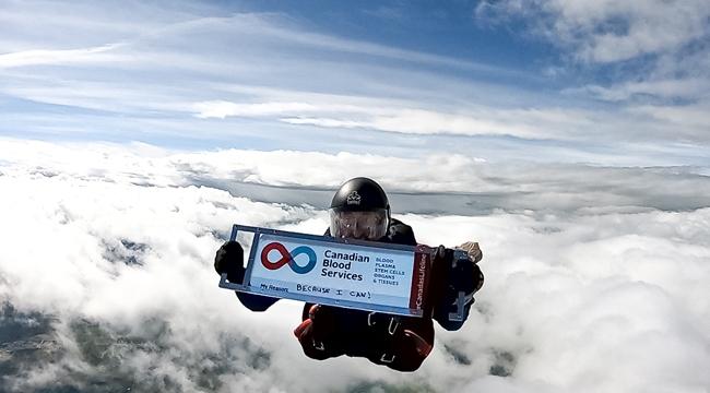 Image of Ian Harrop holding up a sign of Canadian Blood Services of his 600th blood donation while skydiving