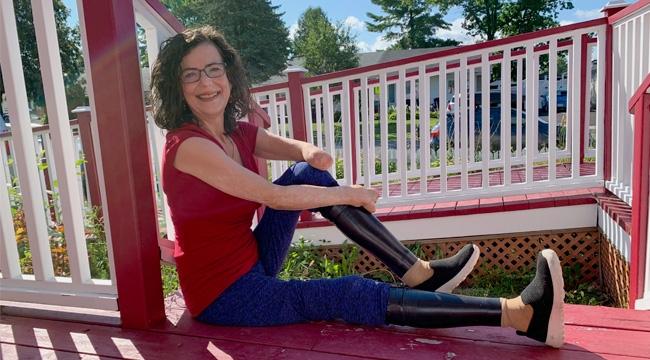 A woman with prosthetic legs sits on her front porch near a wheelchair ramp.