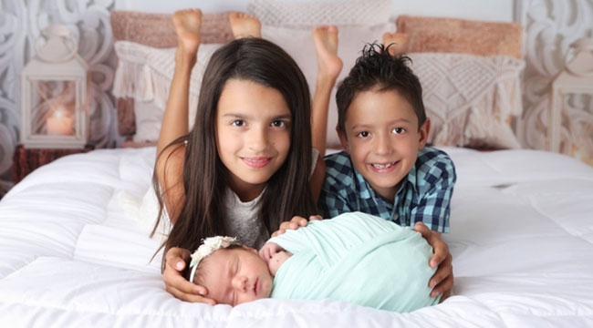 Two children pose with their baby sister