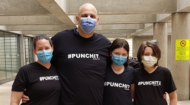 Stem cell recipient Greg Duerksen and his family give each other a side hug in front of his hospital.