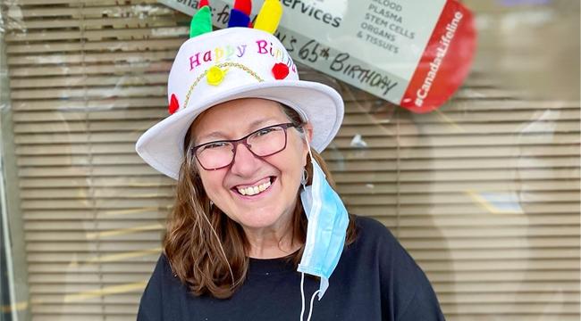 Thumbnail headshot image of Helen Raymond at her blood donor event smiling wearing birthday hat in front of a window