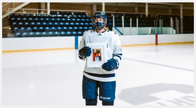 Image of Julia Schmitt holding up a picture frame of her and her dad wearing hockey equipment in an indoor hockey rink.