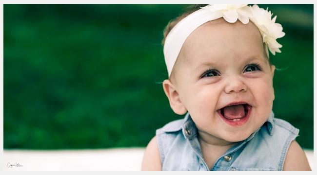 Thumbnail image of baby blood recipient Madison Lewis smiling outside with a flower headband