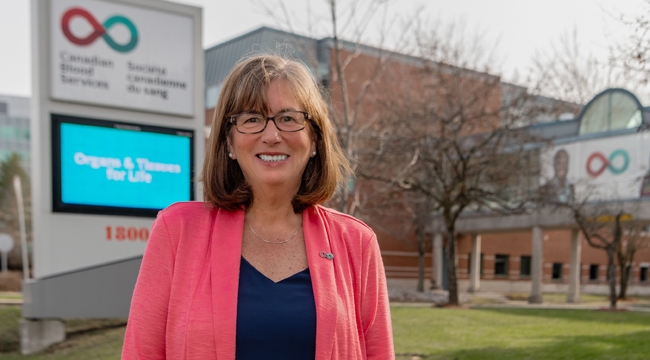 Image of Margaret Miedema, director of philanthropy standing outside of Canadian Blood Services head office's front entrance in front of the signage