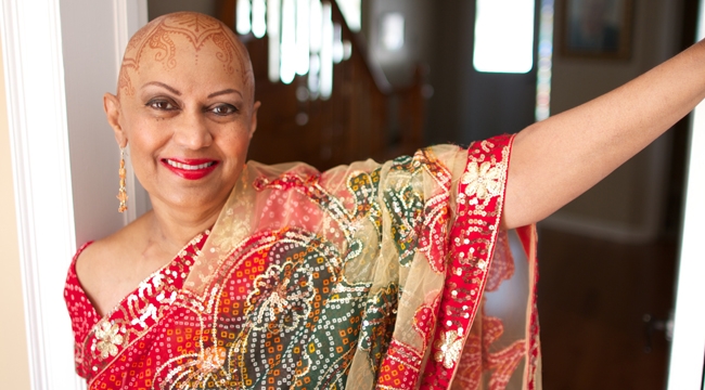 A woman who had blood transfusion procedures during treatment for three different types of cancer stands in a doorway. Her head is painted with a henna design.