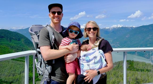 Dressed in casual outfits, Tyler and Rebecca Munk hang out with their toddler and baby on a bridge in Squamish, B.C.