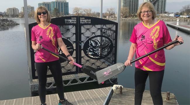 Breast cancer survivors and dragon boat team members Vonnie Pope and Donna Jelly with paddles near the water.