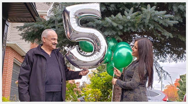 Thumbnail image of Jenn and Tony outside on the lawn looking at each other while holding numbered balloons