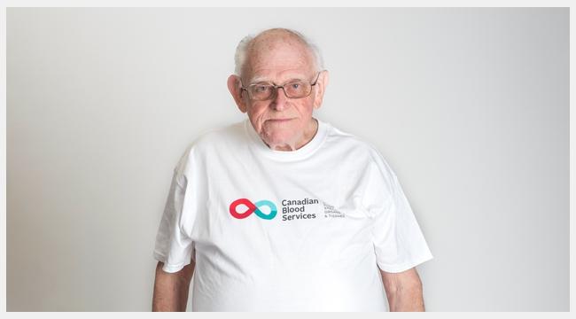 Thumbnail image of Bob Kerr wearing a Canadian Blood Services T-shirt standing in front of a white wall.