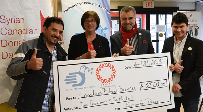 4 people standing and holding a cheque made out to Canadian Blood Services for 2500 as part of Syrian Canadian Donation Day